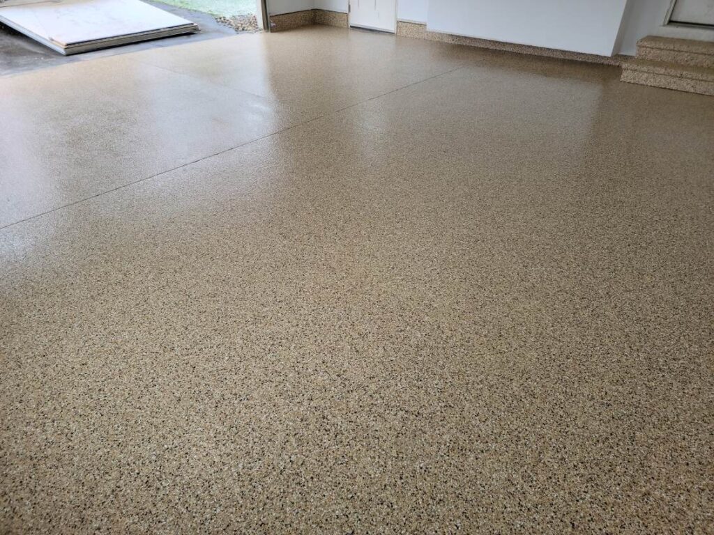 A polished, tan-speckled epoxy floor in an empty interior space, featuring a step and white walls, with no visible furniture or decor.