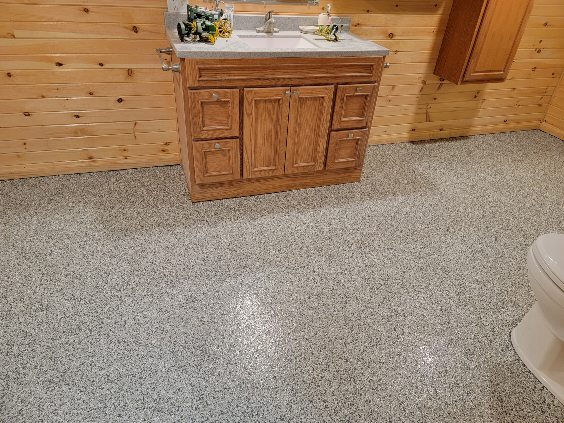 The image features a wooden vanity with a sink, surrounded by wood-paneled walls and a speckled gray floor in a bathroom setting.