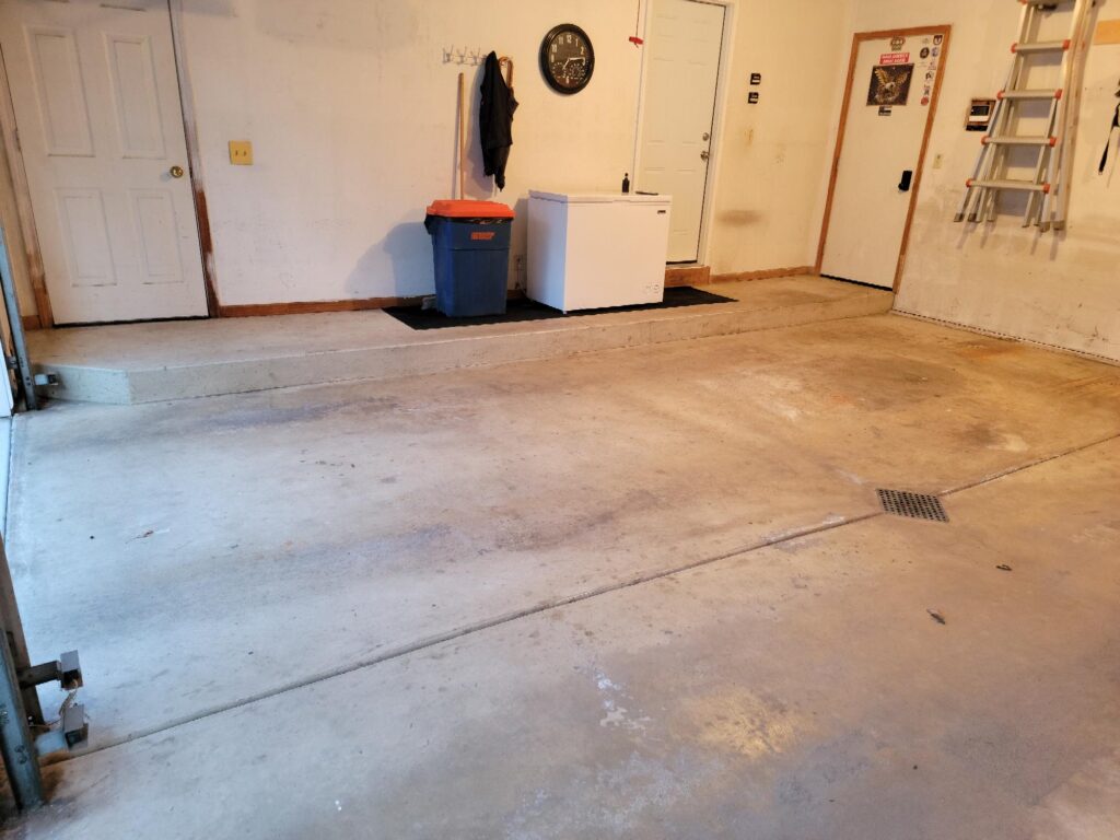 A clean, empty garage with a white freezer, a blue trash bin, and a ladder on the wall. Doors lead to interior spaces.