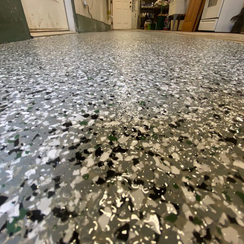 Close-up of a speckled epoxy-coated garage floor with various tools and supplies along the walls in a workspace setting, creating a textured appearance.