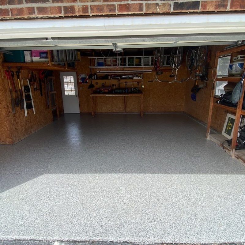 A clean, organized garage with shelves, tools, and bicycles. Storage boxes are neatly arranged on wooden shelves. Bright daylight illuminates the space.