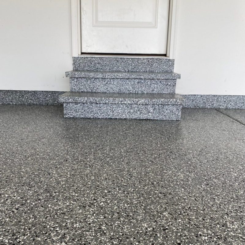 A white door with three speckled gray granite steps leading up to it, against a plain wall, with a circular wall decoration.